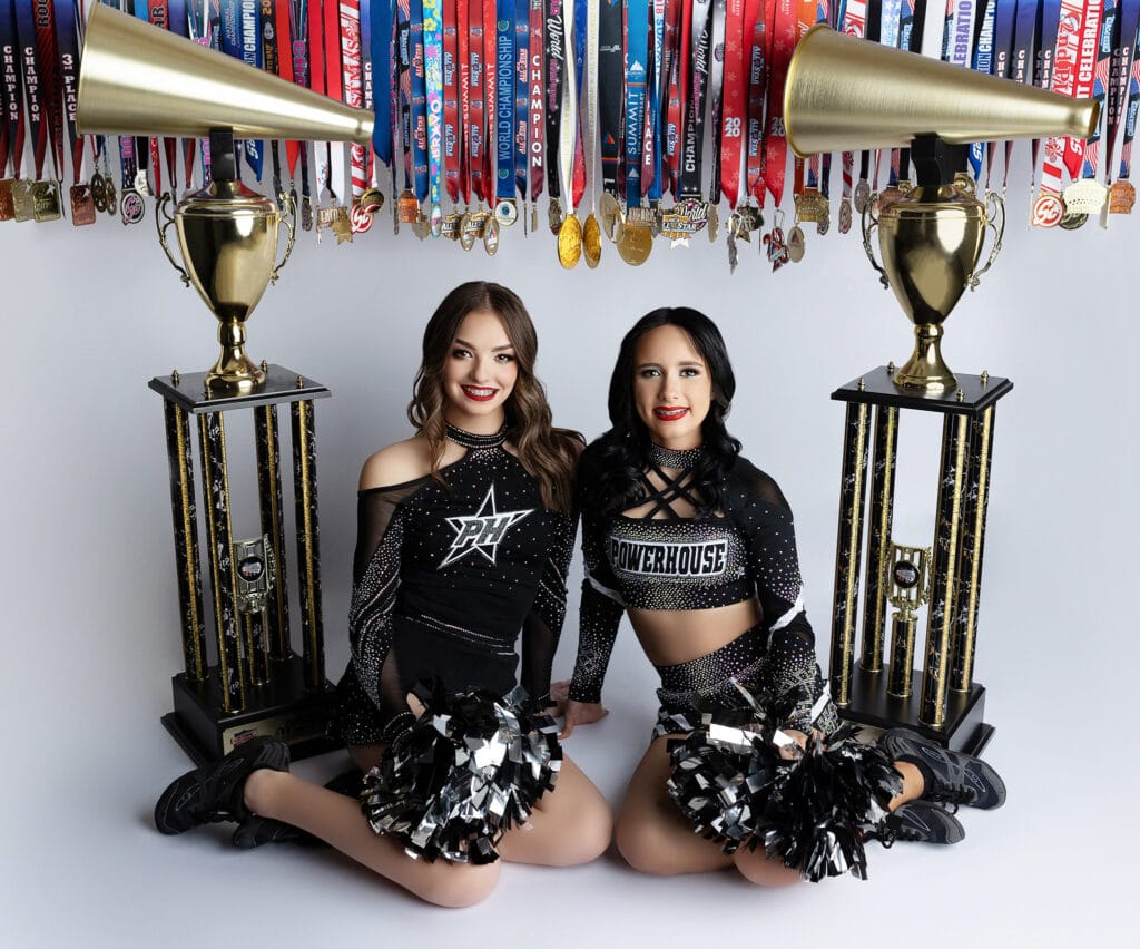 Two cheerleaders with their medals and national championship trophies.