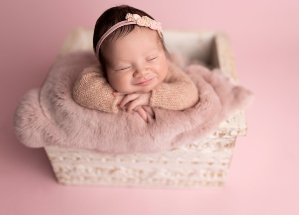 Newborn baby girl smiling on a white antique prop captured by Austin newborn photographer.