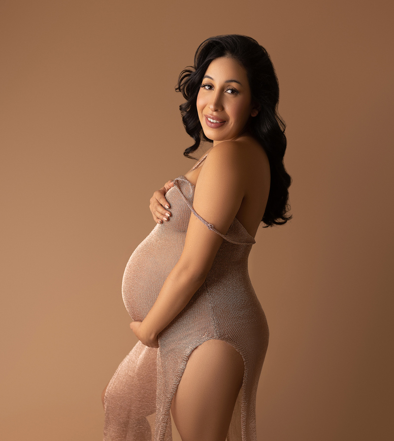 Pregnant woman holding her bump on a rose gold dress.