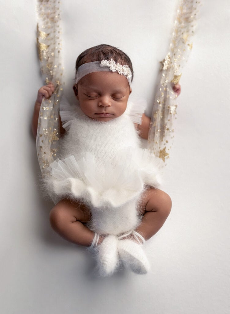 Newborn baby on a ballerina outfit holding on to a swing captured by Austin, Texas newborn photographer.